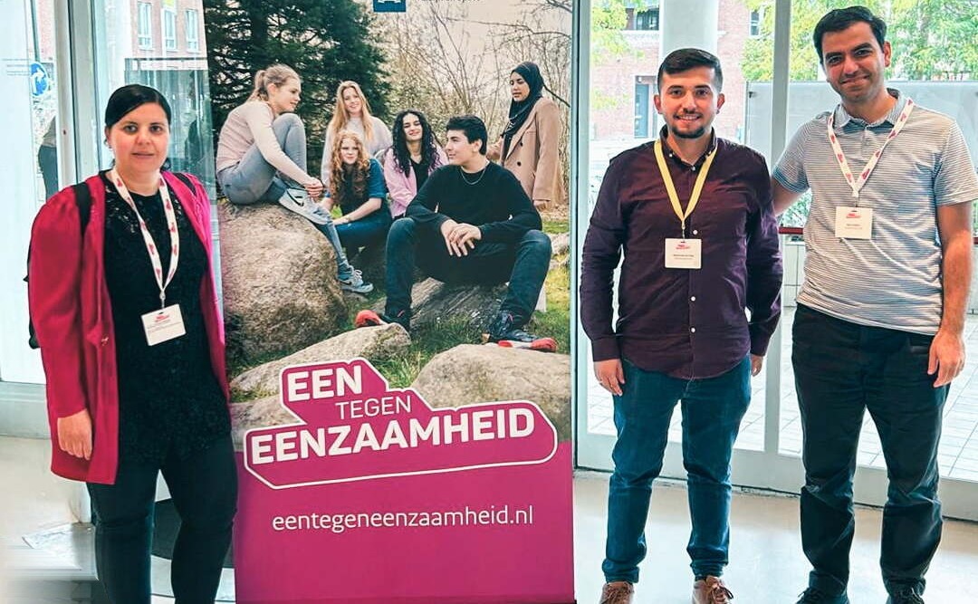 Drie deelnemers naast een banner van Eén tegen eenzaamheid